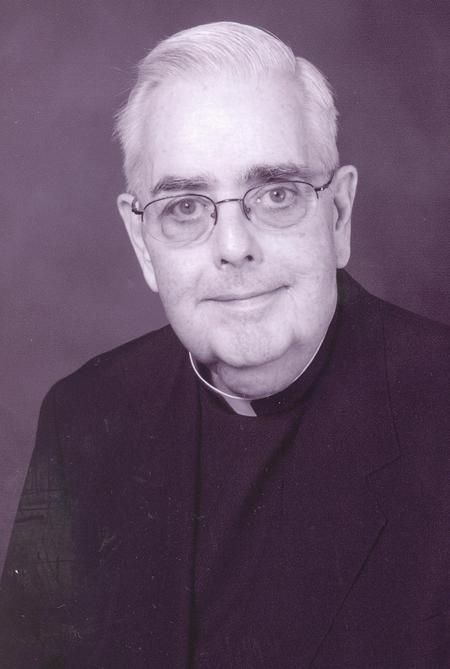 Blue-tinted black and white portrait-style photograph of Thomas Gannon, an old, white man, clean shaven, wearing glasses, dressed in a black priest robe with a white, Roman collar.